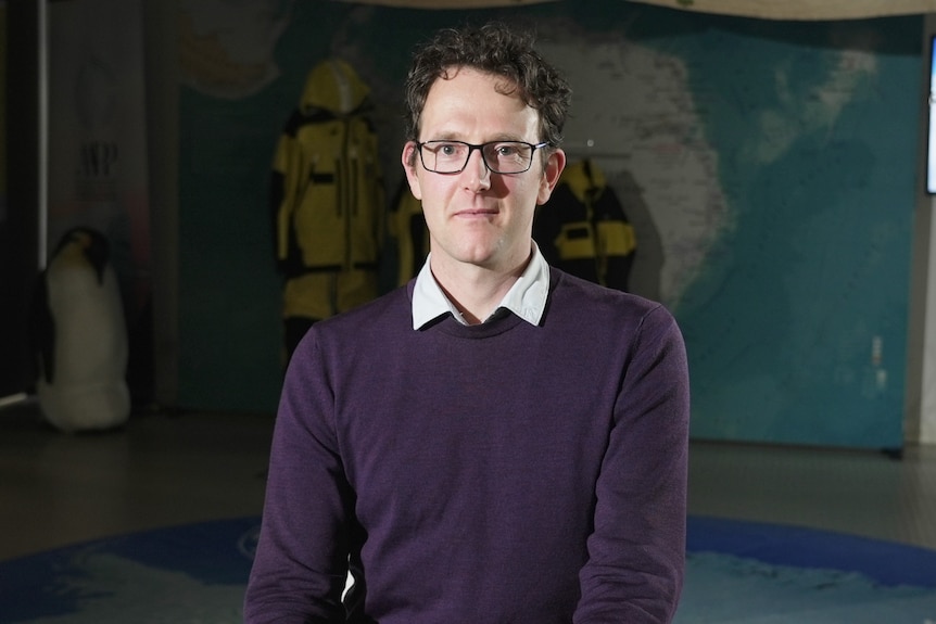 Physical oceanographer Edward Doddridge looks at the camera with a giant map on wall behind him.