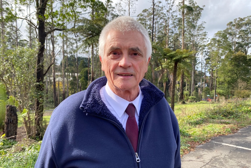 Jim Child, wearing a blue fleece jacket as he stands in front of Dandenong Ranges rainforest.