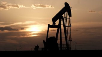 An oil pump is seen as a silhouette in front of an orange sunset.