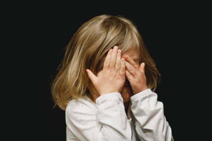 a little girl covers her face with her hands.