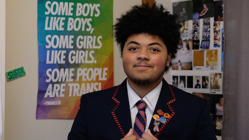 Jamil stands in his room in his school uniform. An LGBTQIA poster is in the background.