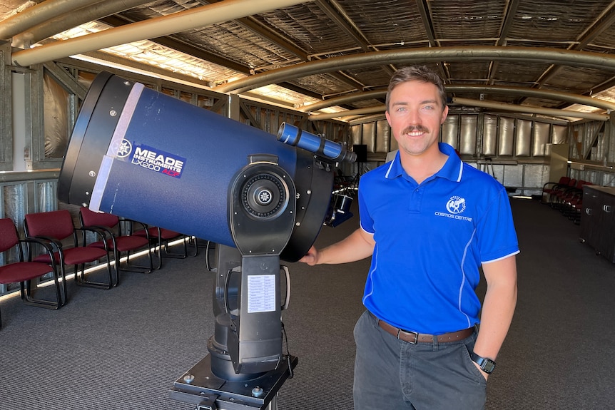 A man in a blue shirt smiling at camera with a large telescope.
