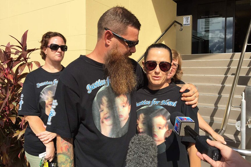 A bearded man and a dark-haired woman, wearing matching T-shirts, stand outside a court building.