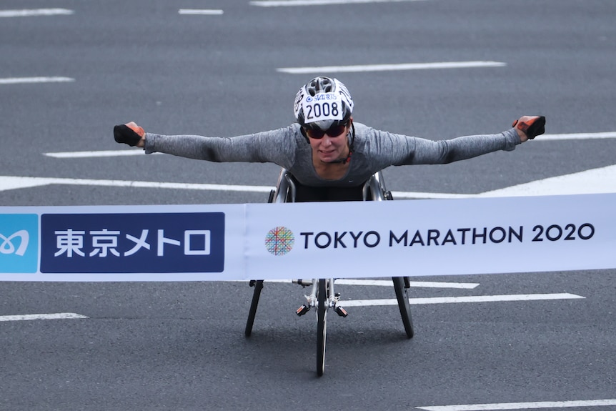 Christie Dawes holds her arms out and wheels into the finishing banner.