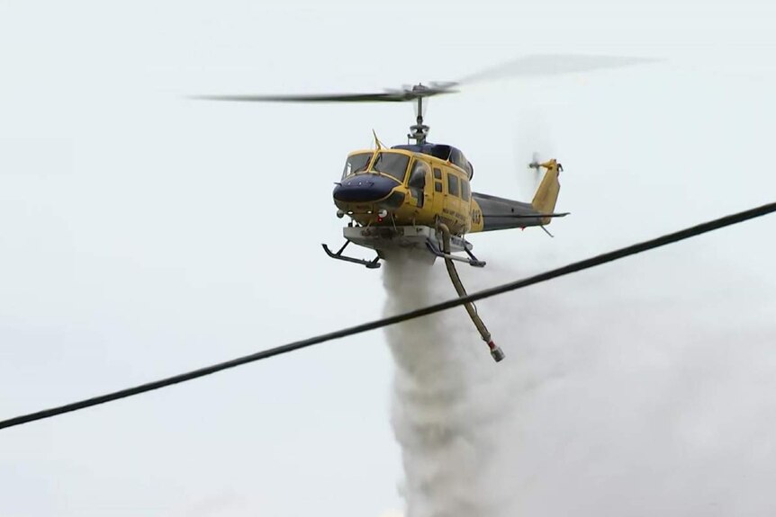 A helicopter drops water on a bushfire