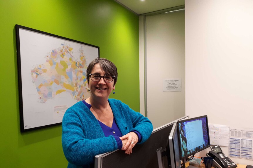A woman leans on a office cubicle in front of a map of Australia.