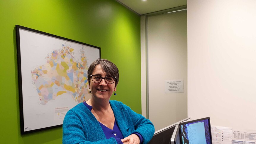 A woman leans on a office cubicle in front of a map of Australia.