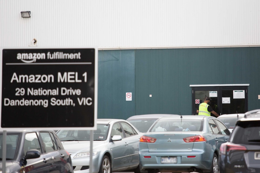 A man wearing a yellow Adecco vest and a cap enters the front door of the Amazon fulfillment centre.