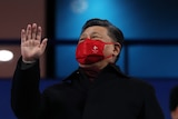 Xi Jinping waves while wearing a red face mask with the Beijing Olympics logo on it