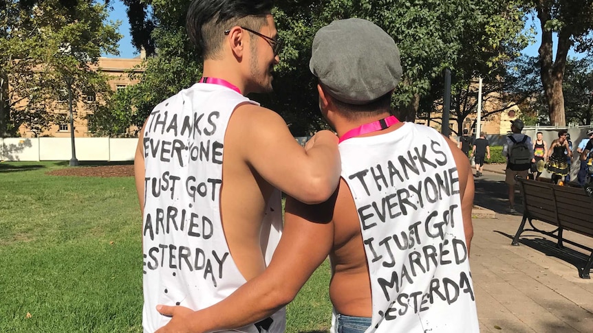 Two men wearing tank tops and showing their back, which states that they got married yesterday.