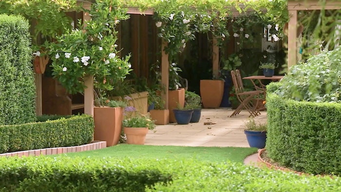 Garden filled trimmed hedges, large pots and courtyard in background