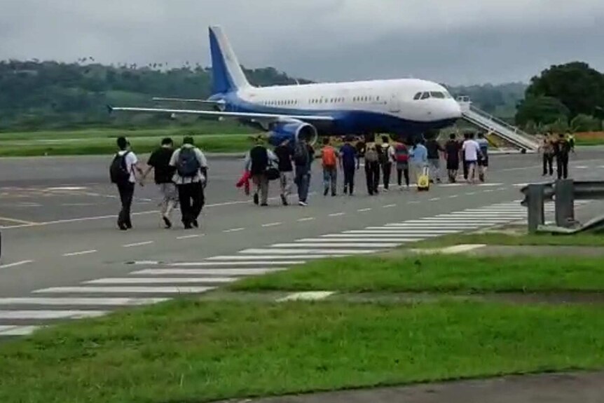 Six Chinese nationals are escorted along the tarmac and onto a plane at Port Vila airport