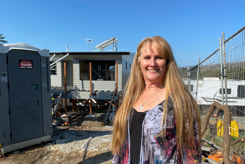 Katrina Walsh stands smiling out the front of her home, which is under construction behind her.