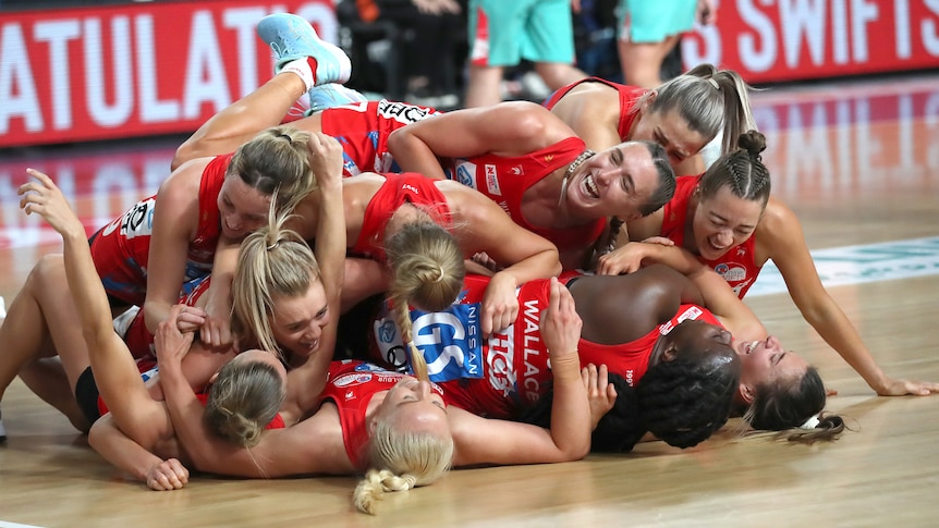 NSW Swifts players pile on each other on the court, laughing and smiling