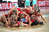NSW Swifts players pile on each other on the court, laughing and smiling