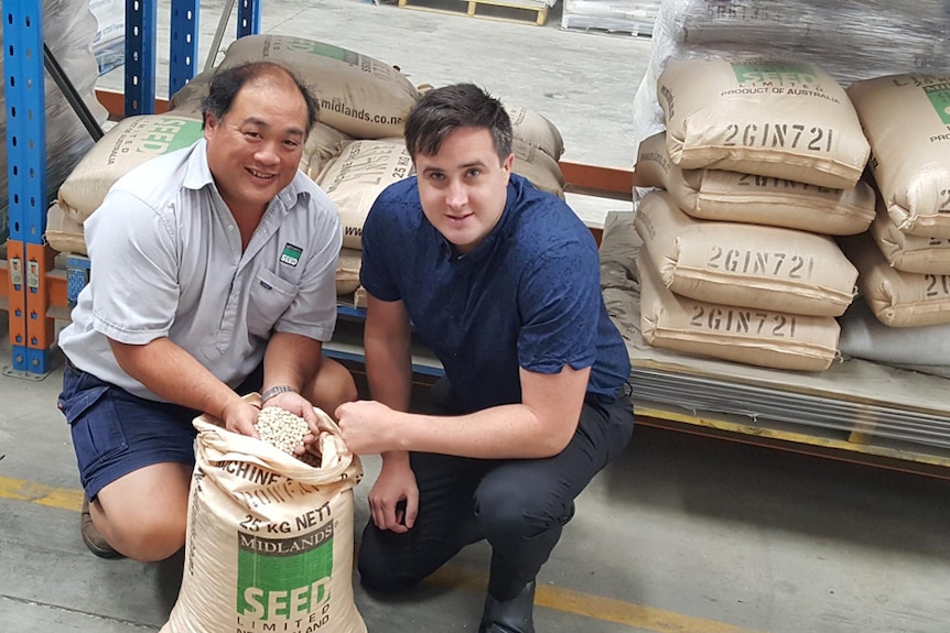 Two men crouch down to show off a bag of marrowfat peas.