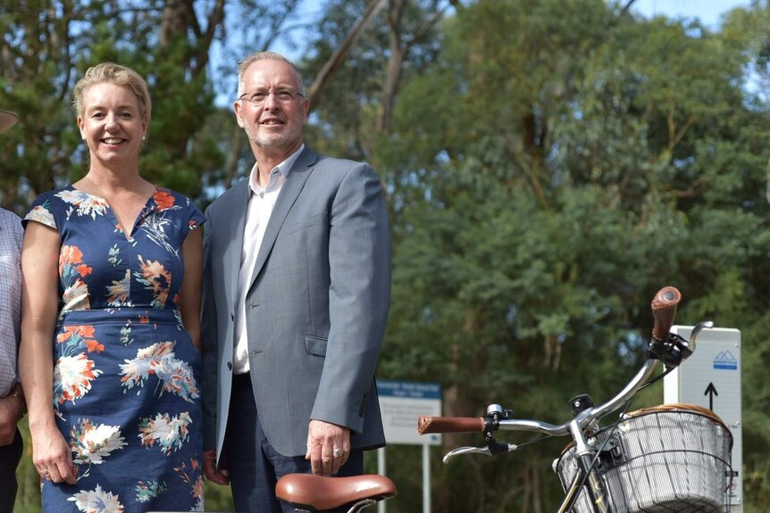 A woman and man stand next to a bicycle.