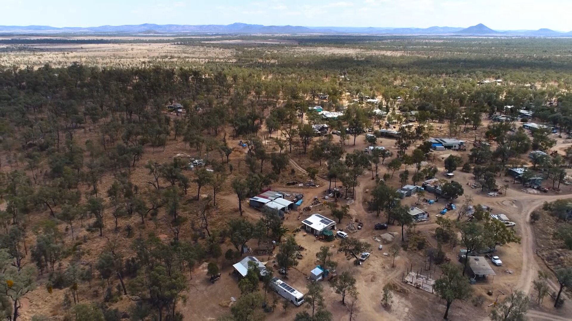 Aerial photo of about a dozen shacks dotted among red dirt roads and scrub
