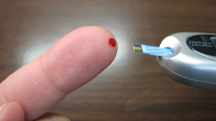 Human finger with blood spot being used to gauge blood sugar level