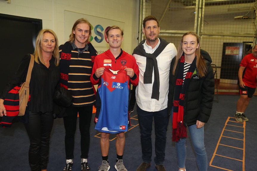 Charlie Spargo (centre) holds up his first Melbourne Demons AFL jersey. His parents and siblings stand with him.