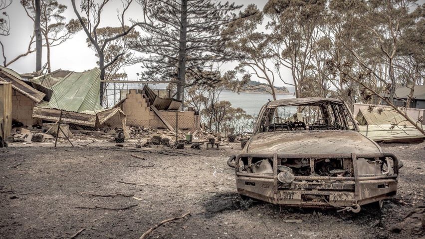 a burnt out car in front of a destroyed home