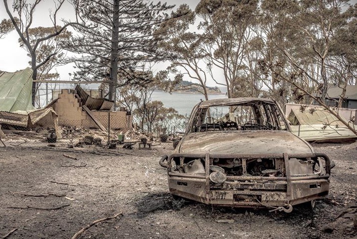 A burnt-out car in front of a destroyed home.