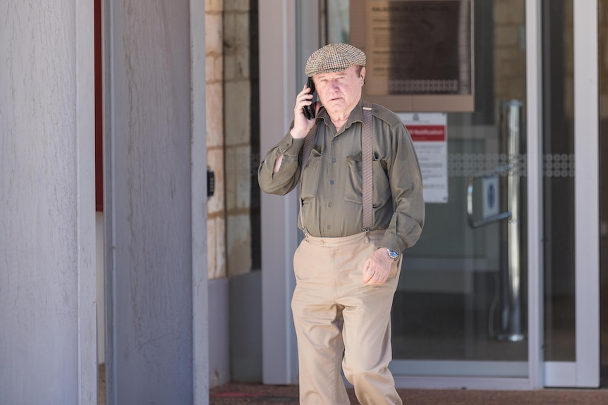 A man on a mobile phone walking out of a courthouse. 