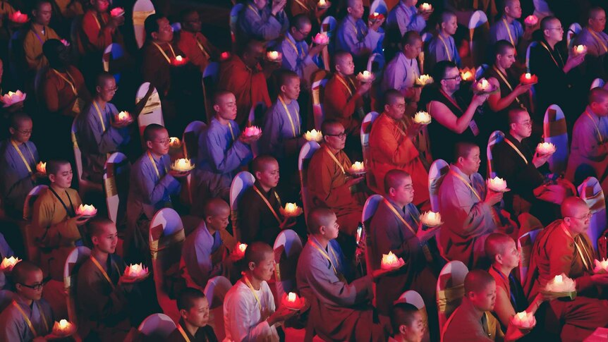 A crowd of seated monks holding lotus shaped candles.