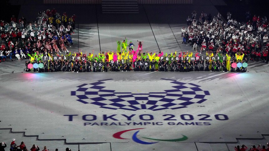Performers hold signs saying "thank you to all the Paralympians" as the stand in front of the Tokyo 2020 Paralympics logo 