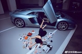 A woman lies flat on the ground with cash and make up scattered around her. It looks like she has fallen out from a sports car.