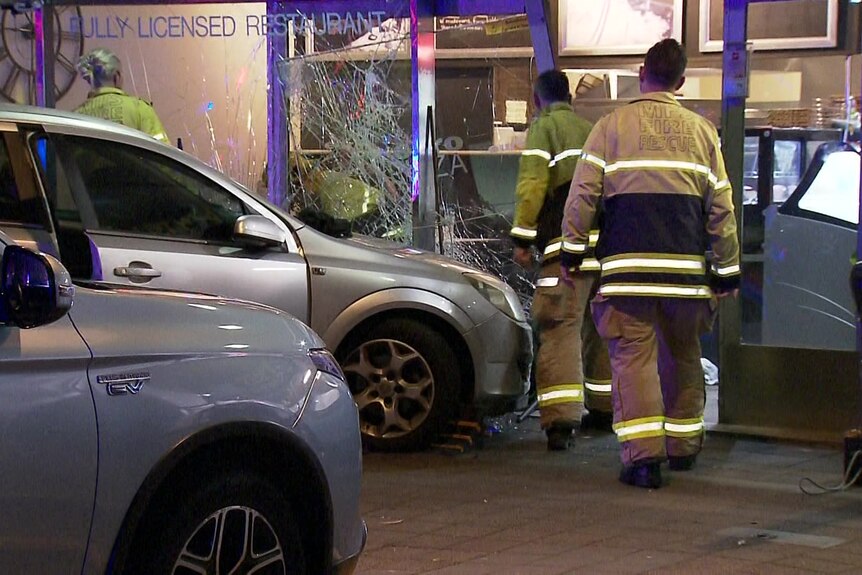 Firefighters next to a car that smashed glass windows of a restaurant