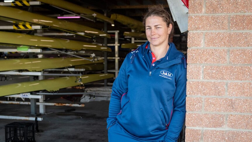 A woman leans against the wall of a boat shed.
