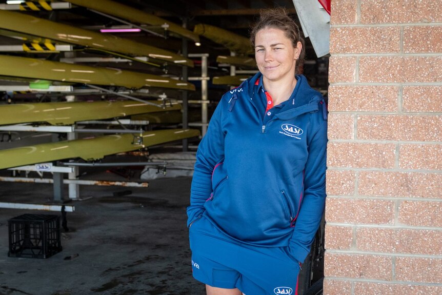 A woman leans against the wall of a boat shed.