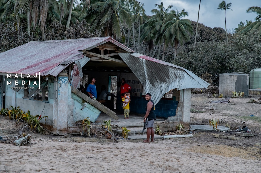 Young people stand near and in a dilapidated home after the Tongan eruption and tsunami. 