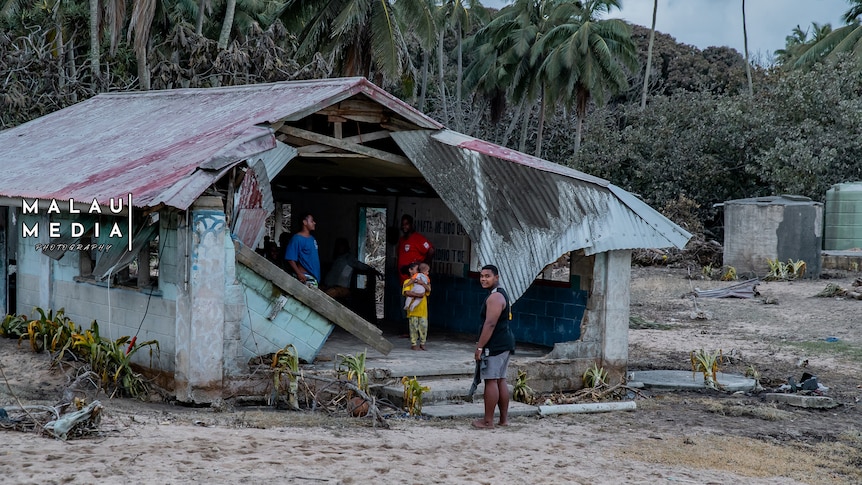 Young people stand near and in a dilapidated home after the Tongan eruption and tsunami. 
