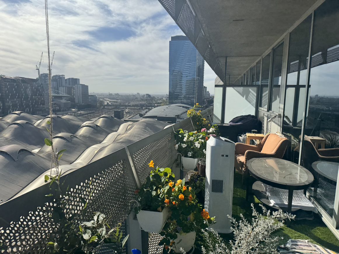 The undulating roof of Southern Cross can be seen adjacent to a balcony with plants.