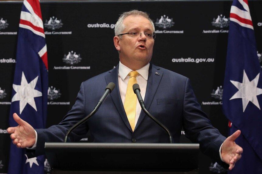 Scott Morrison speaks at a press conference, flanked by Australian flags.