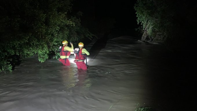 Two firefighters wade through flood water at night