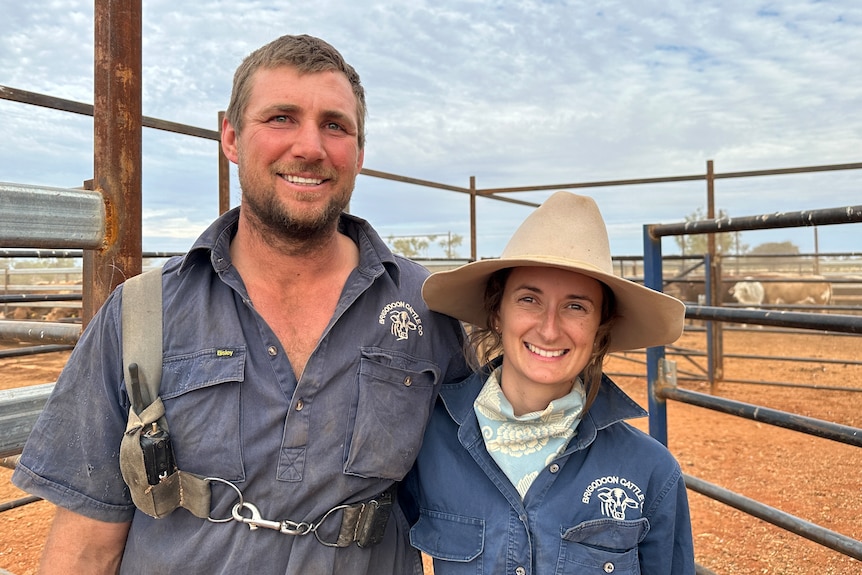 A man and a woman stand in a dusty set of cattle yards