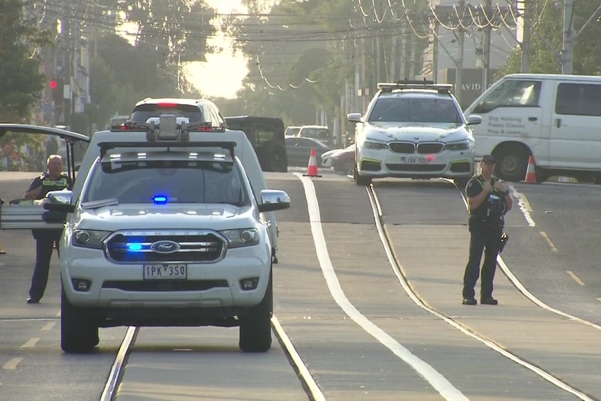 Two police cars with lights on parked across tram tracks with officers in uniform standing around. 