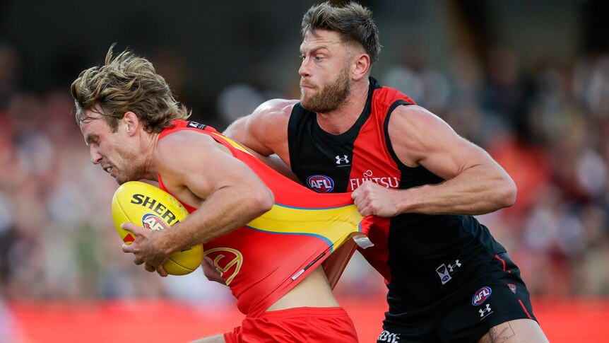A Gold Coast Suns AFL player is tackled by an Essendon opponent.
