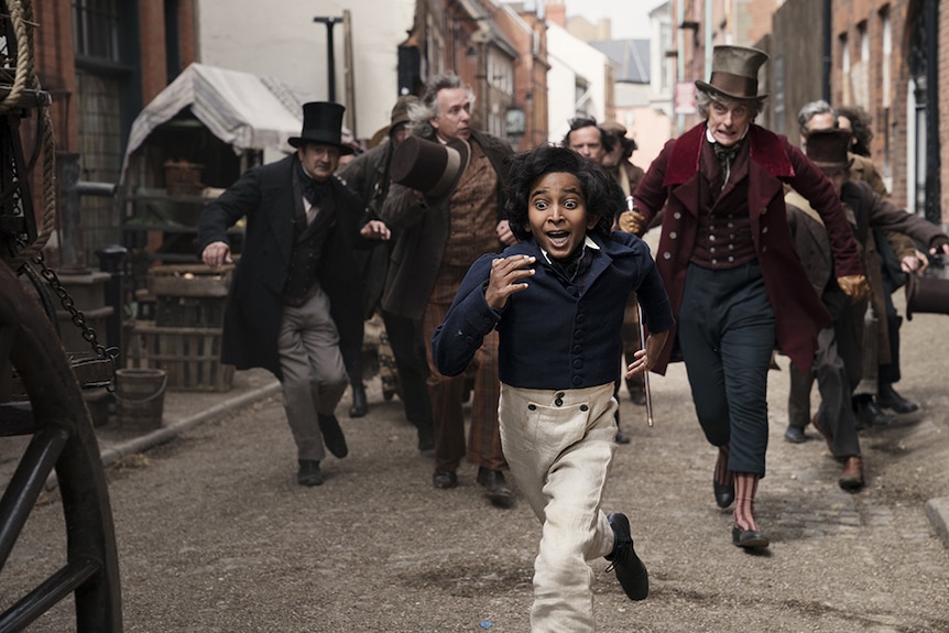 In Victorian era England a young boy with fearful expression runs down street chased by group of suited and top hatted men.