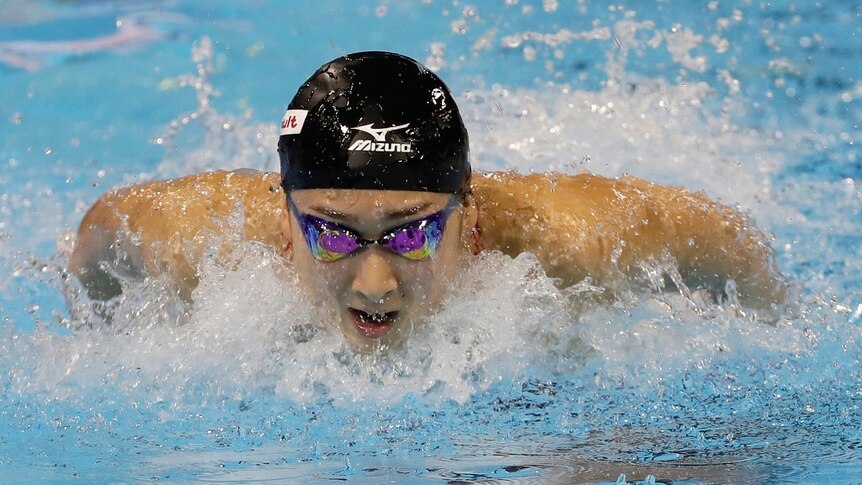 A swimmer wearing a swimming cap and goggles rises from the water and breaths mid stroke.