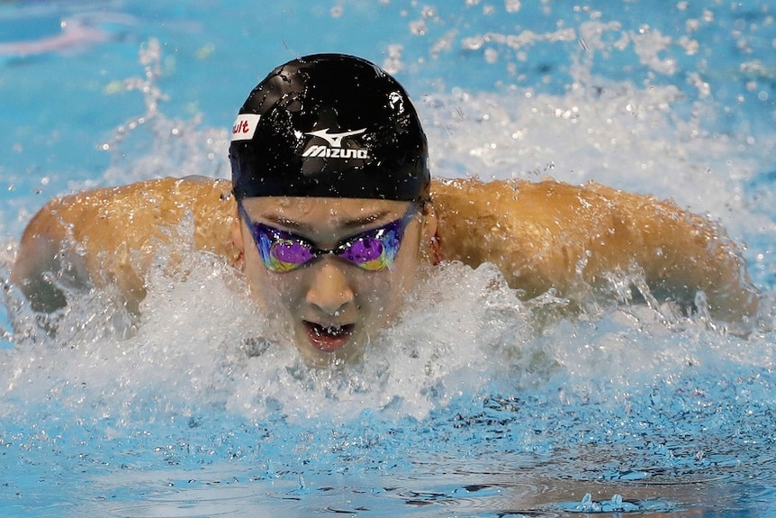 A swimmer wearing a swimming cap and goggles rises from the water and breaths mid stroke.