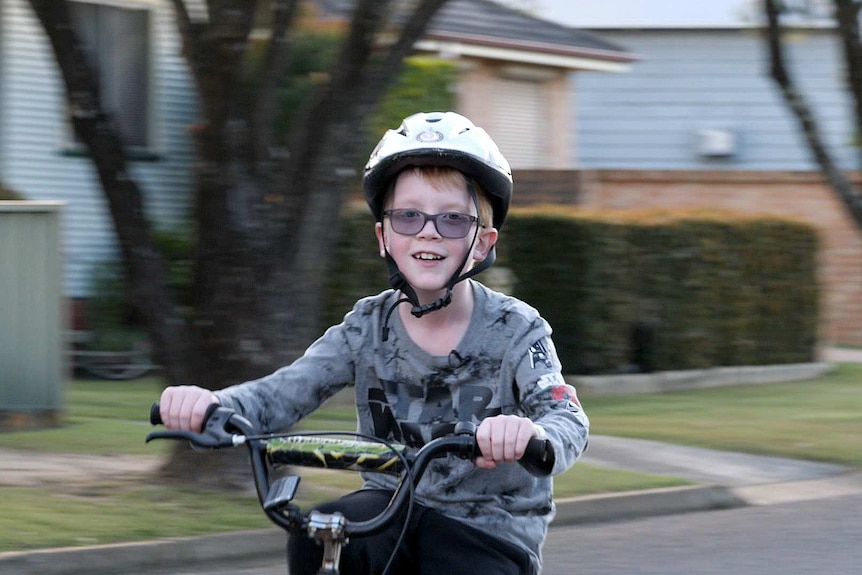A boy in a white helmet riding his bike and smiling at the camera