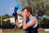 A football player tips water on his head during a hot Darwin day.