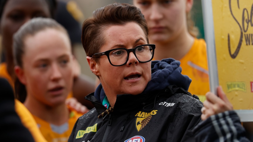 An AFLW coach looks to her left towards players as she delivers a team talk during a break in a game.
