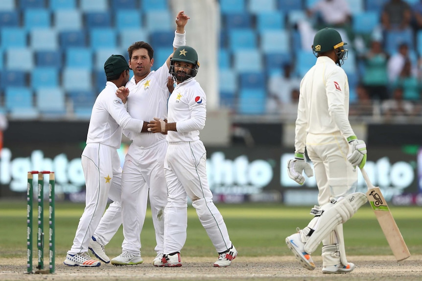 Wide shot of four cricketers in action on the field.