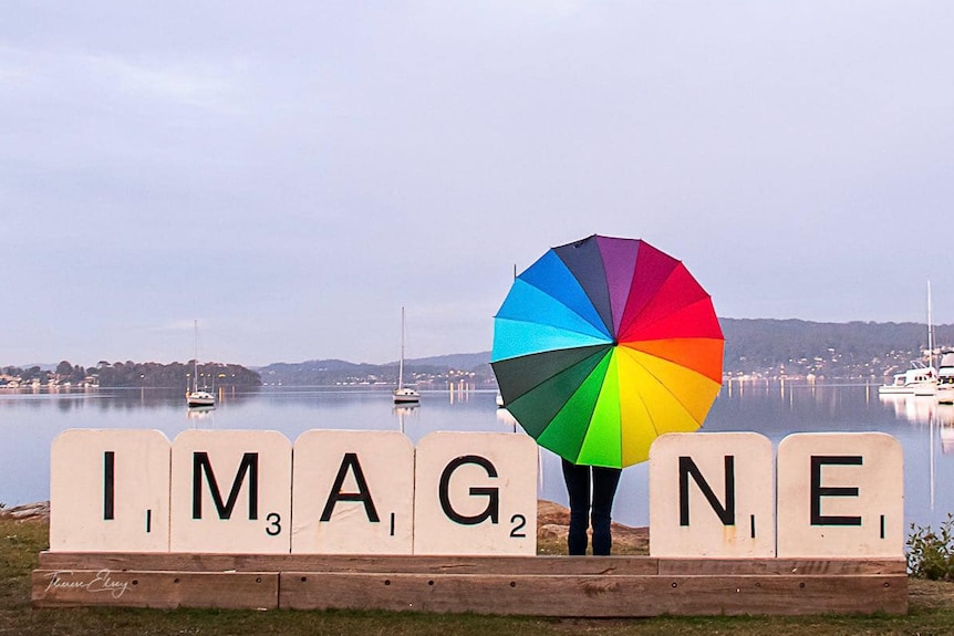 A person with a colourful umbrella poses with a giant sculpture.
