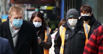 People walking down a Melbourne footpath wearing dark coats and face masks.